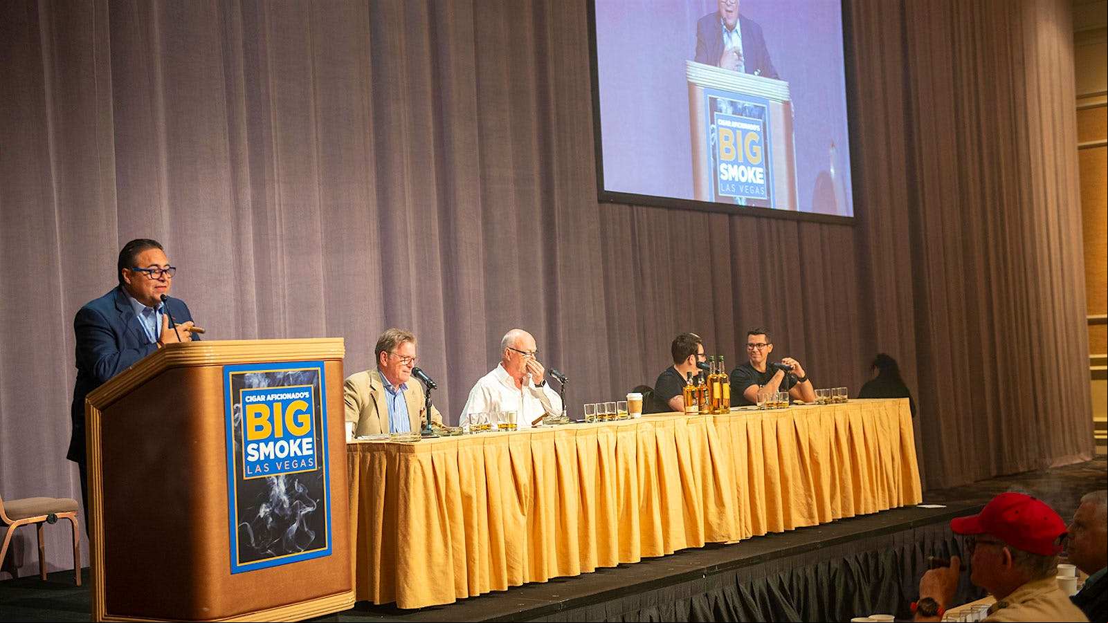 Rafael Nodal (at podium), talking about the H. Upmann being smoked with Tequila and mezcal during the final seminar. At the table, from left: Jack Bettridge, Gordon Mott, Allison Contreras and Alan Ruesga-Pelayo.
